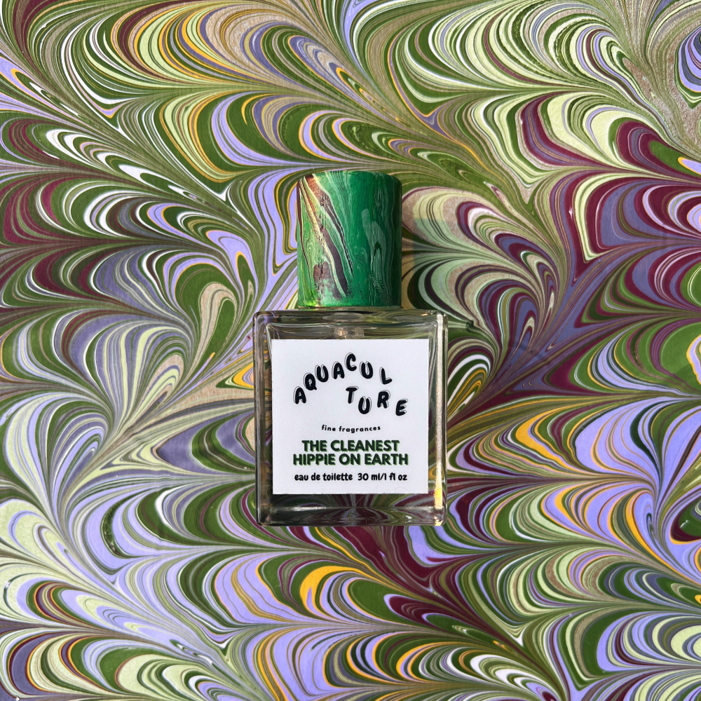 Perfume bottle labeled 'Aquaculture The Cleanest Hippie on Earth' on a marbled background